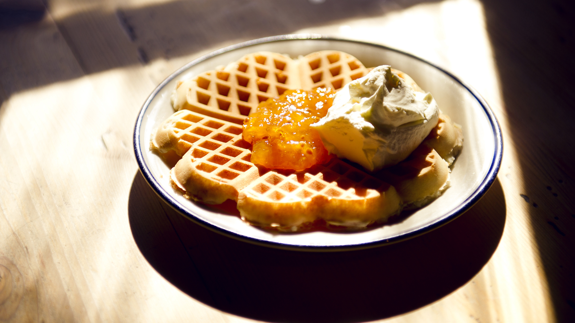 Vafler på en tallerken med syltetøj og flødeskum, serveret på et træbord i modlys