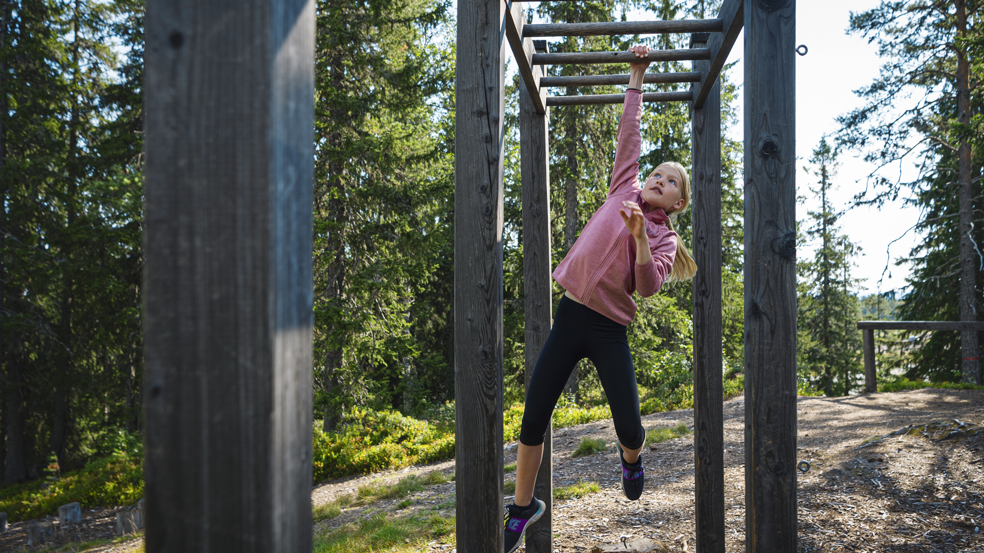Ung pige klatrer på abebar i skoven, iført lyserød trøje og sorte leggings