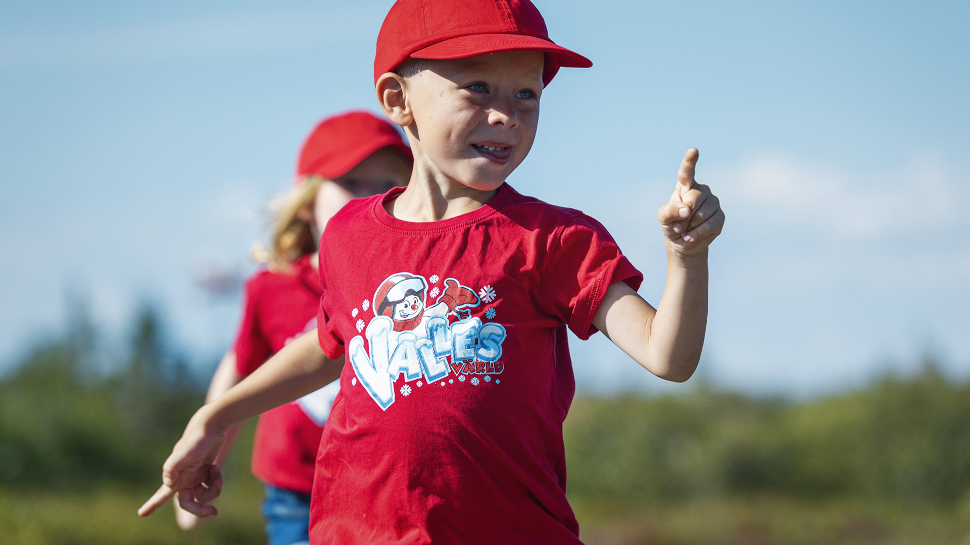 Barn i röd t-shirt och keps med Valter-tema pekar och ler utomhus