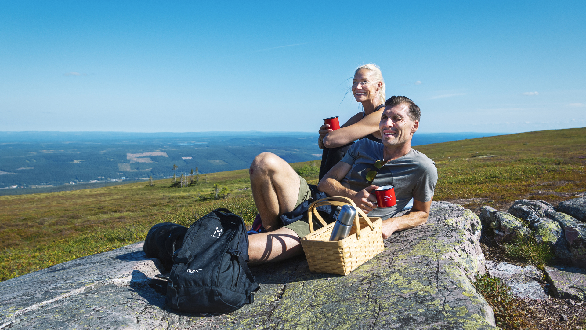 Paar auf einem Picknick in den Bergen, genießt die sonnige Aussicht mit Proviant und Thermoskanne auf einem Stein