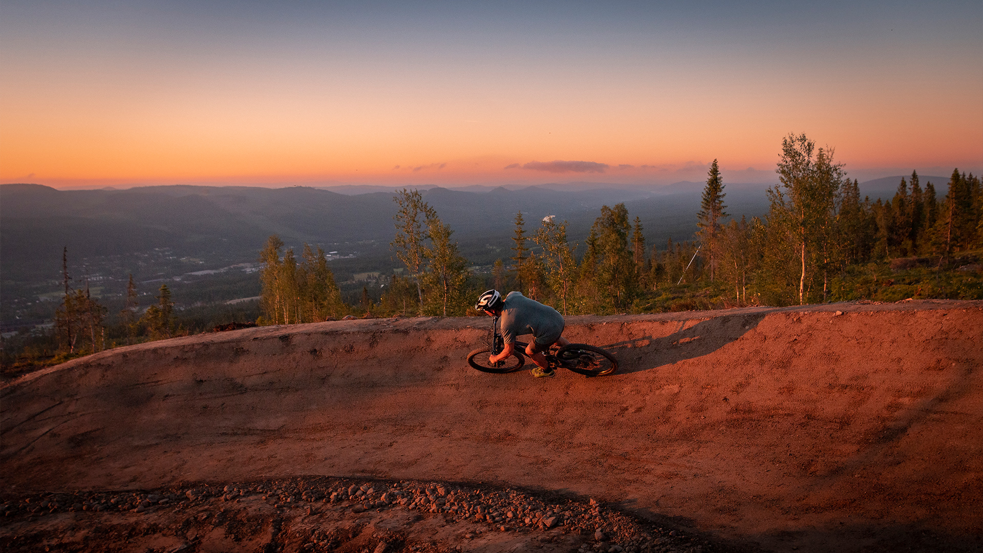 Cyklist på cykelled i solnedgång, omgiven av skog och berg
