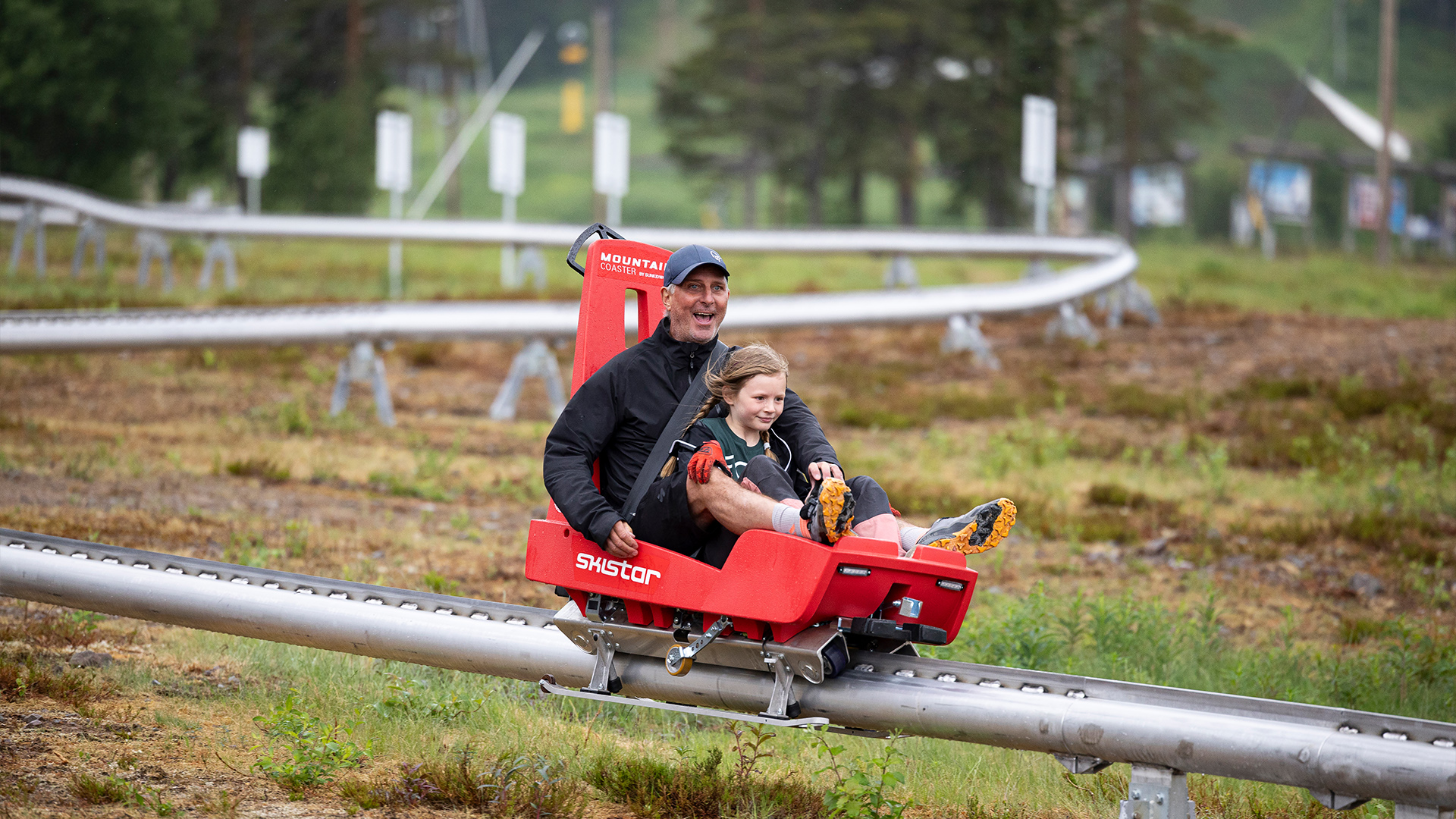 Personer åker Mountain Coaster, en typ av rodelbana, i grönskande landskap, spännande sommaraktivitet i Trysil, Norge