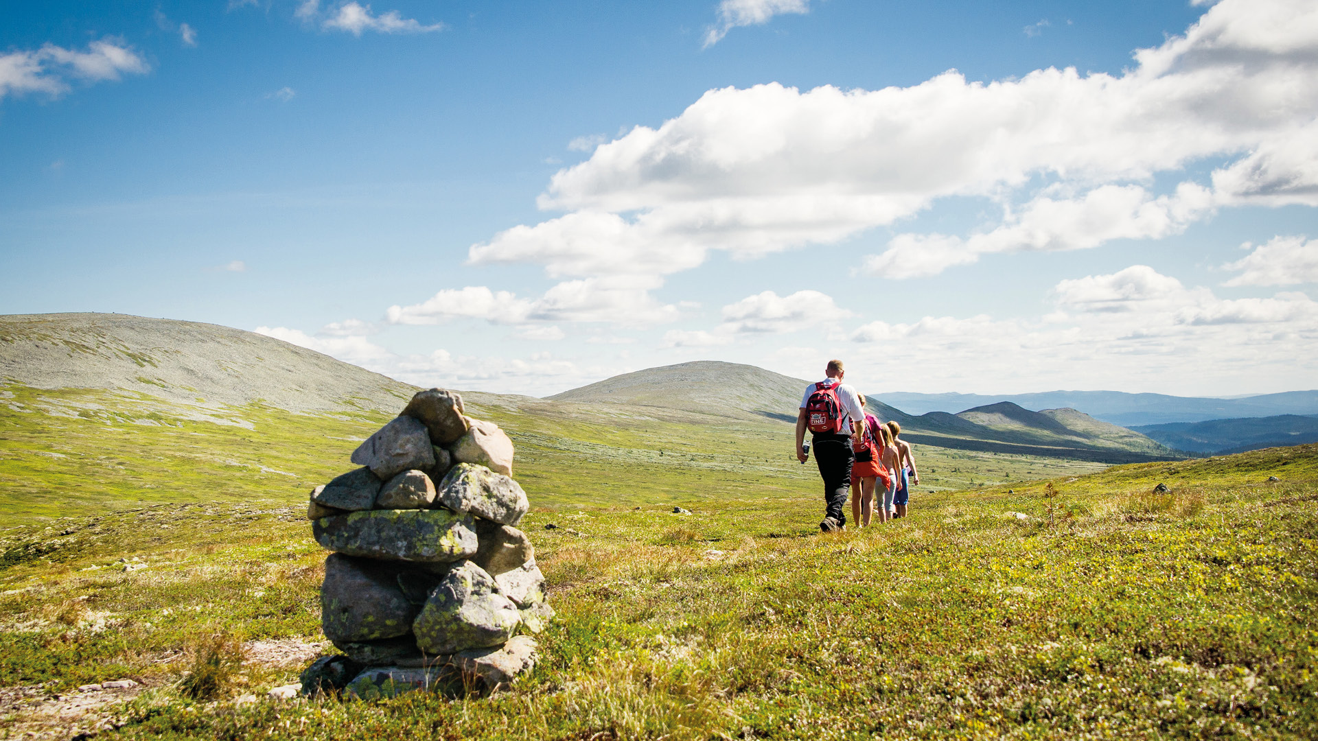 Familie wandert in einer Gebirgslandschaft mit Steinmännchen, blauem Himmel und Wolkenformationen