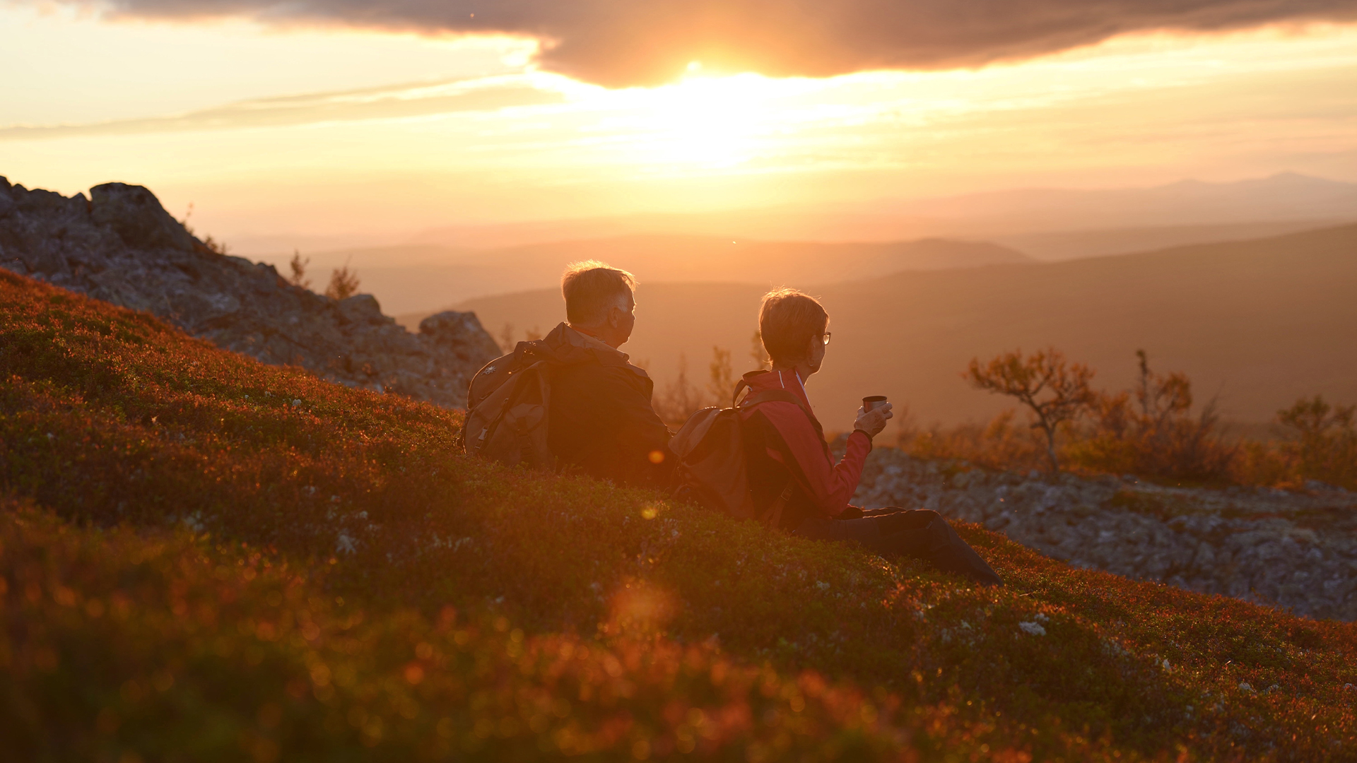Två personer sitter på en bergssluttning i solnedgången och njuter av den natursköna utsikten i skogen