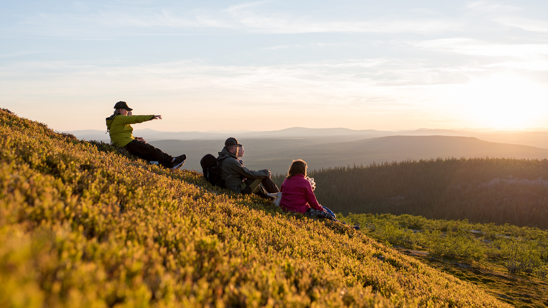 Familie genießt den Sonnenuntergang auf einem Hügel mit Blick auf Wald und Berge in Schweden