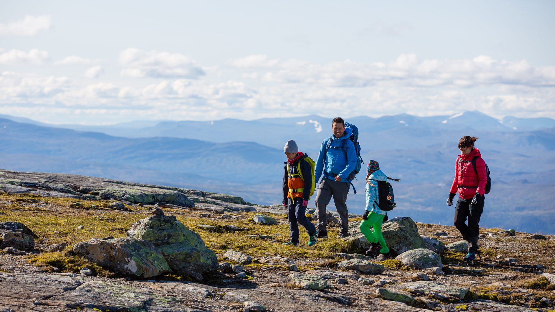 Vandring i fjällen med fyra personer i färgglada jackor, klara himmel och berg i bakgrunden