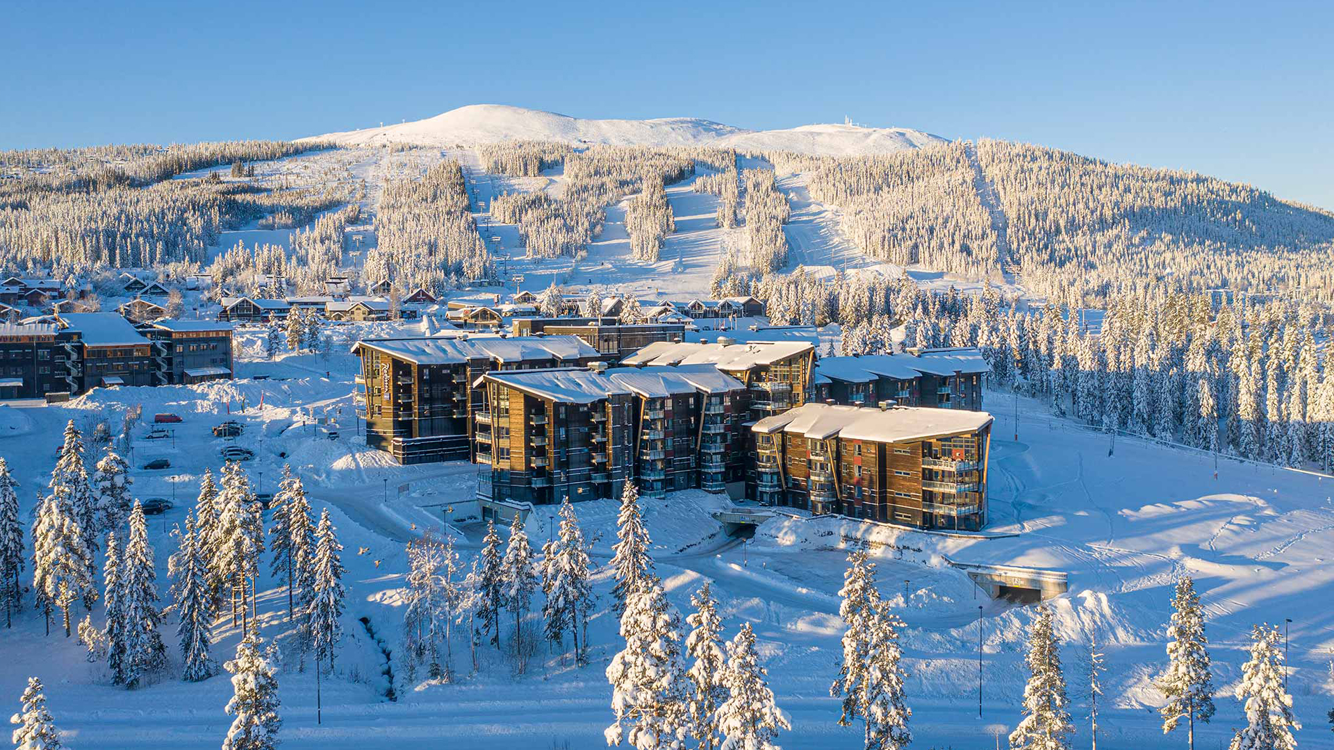 Vinterlandskap med moderne leiligheter i et snødekt fjellområde i Trysil, Norge, med skibakker og skoger i bakgrunnen